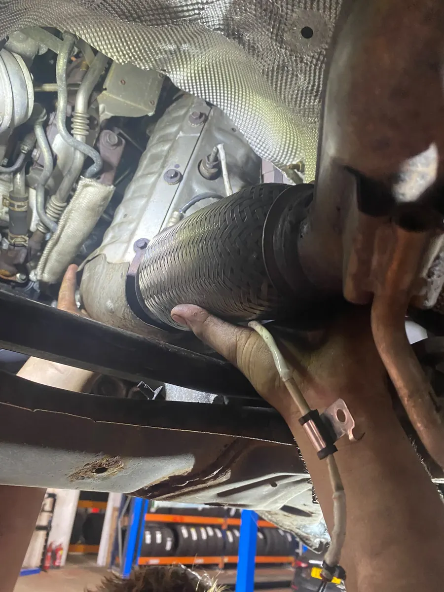 Technician positioning the cleaned DPF and exhaust flexi-pipe under the vehicle