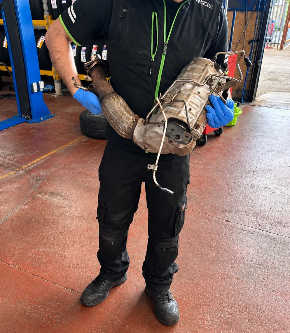 247 Autocentre technician holding a complete removed DPF and exhaust assembly in the Cwmbran workshop